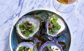 a plate of oysters with a glass of wine and some herbs on the side at Fretheim Hotel