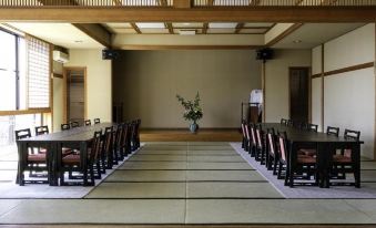 a large room with a wooden ceiling and tatami mats , featuring a long table surrounded by chairs at Ryokan Warabino