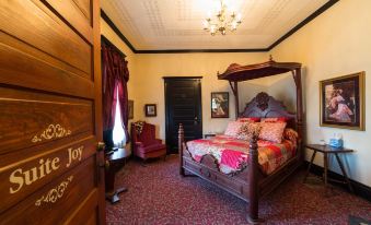 a cozy bedroom with a wooden bed , red curtains , and a chandelier hanging from the ceiling at Grand Victorian Inn