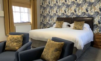 a large bed with white linens and two blue chairs in front of a window at The Red Lion Inn
