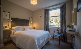 a well - lit hotel room with a large bed , white bedding , and a window looking out onto a mountainous landscape at Chestnut Villa