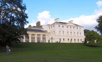 a large white building with a green lawn in front of it and trees in the background at Roseview Alexandra Palace Hotel