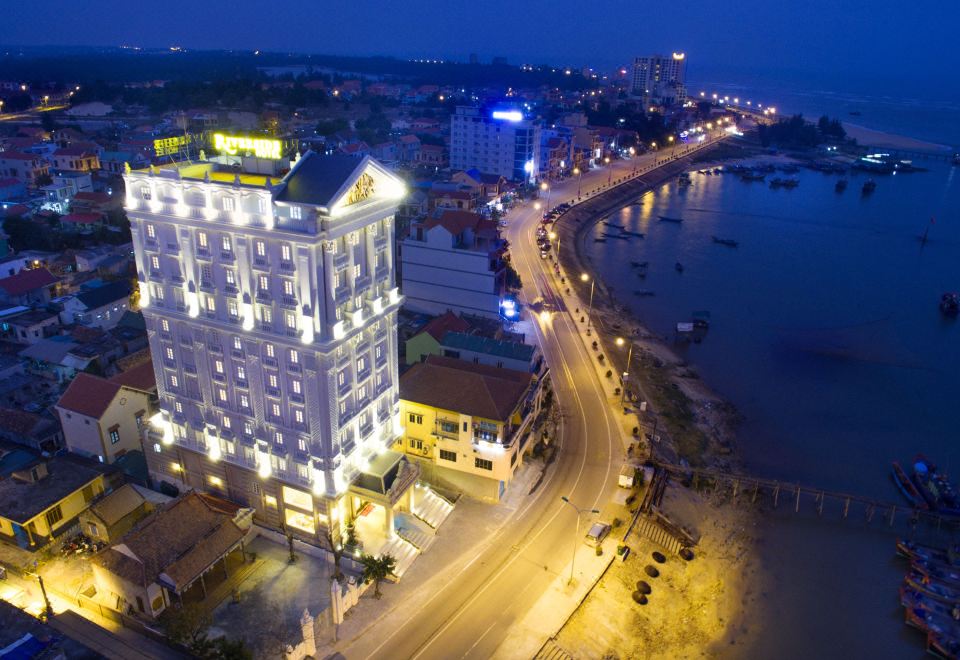 an aerial view of a city at night , with a tall building illuminated in the background at Riverside Hotel Quang Binh