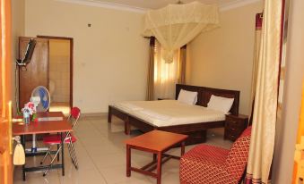 a spacious bedroom with a large bed , a dining table , chairs , and a tv . also a couch in the room at Country Inn Masindi