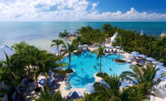 a large outdoor pool surrounded by lounge chairs and umbrellas , with palm trees in the background at Isla Bella Beach Resort & Spa - Florida Keys