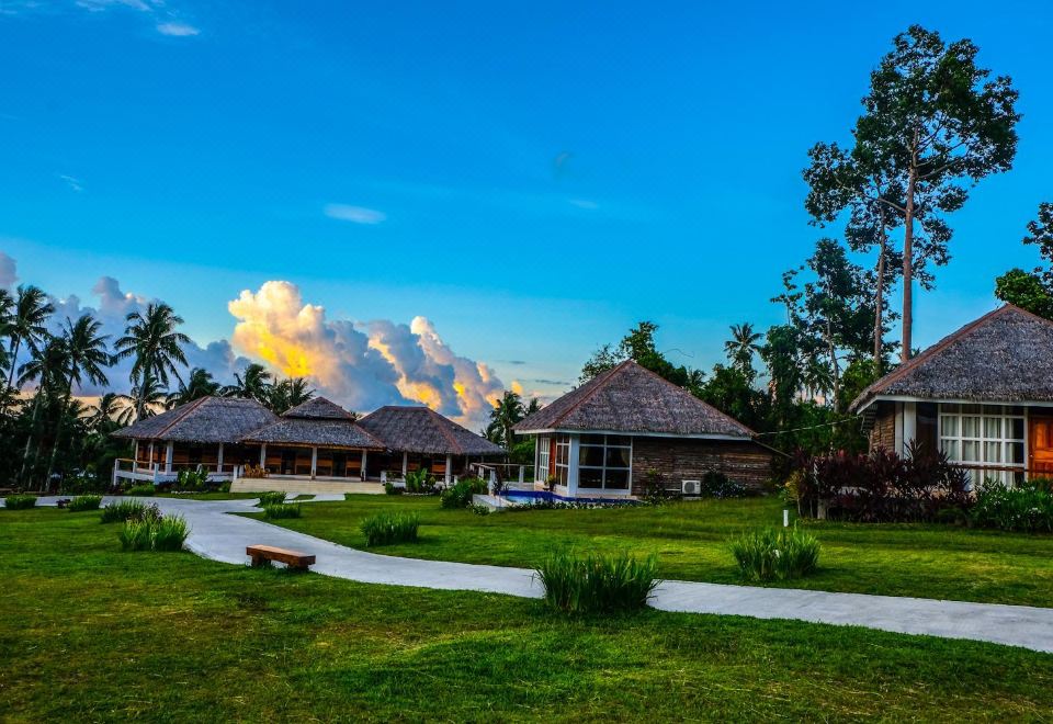 a serene landscape with thatched - roof houses surrounded by lush greenery , set against a clear blue sky and tropical clouds at Recidencia Del Hamor