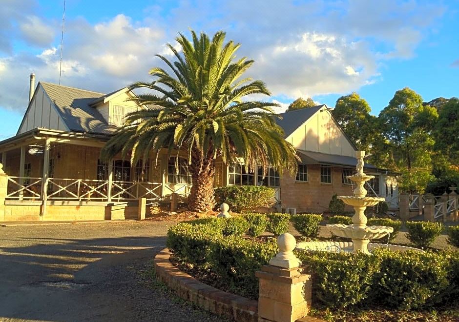 a large house with a palm tree in front of it , surrounded by a lush green garden at Picton Valley Motel Australia