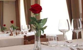 a dining table with a single red rose in a vase , surrounded by wine glasses and cutlery at Hotel Savoia