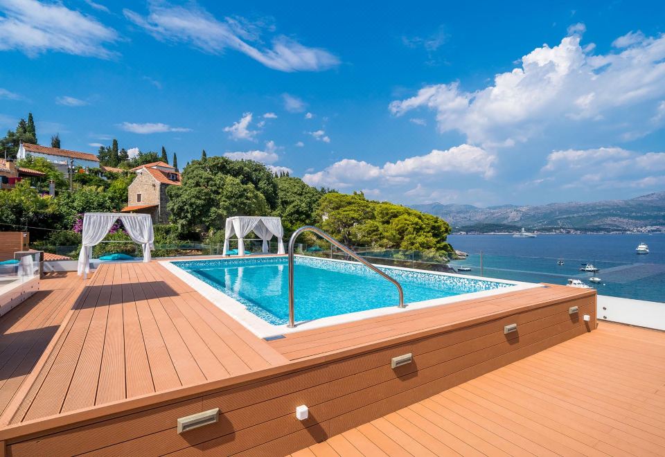 a large swimming pool with a wooden deck and surrounding area of trees and houses at Kalamota Beach House