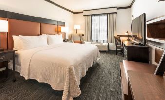 a large bed with white linens is in a room with a desk , chair , and lamp at The Craftsman Inn & Suites