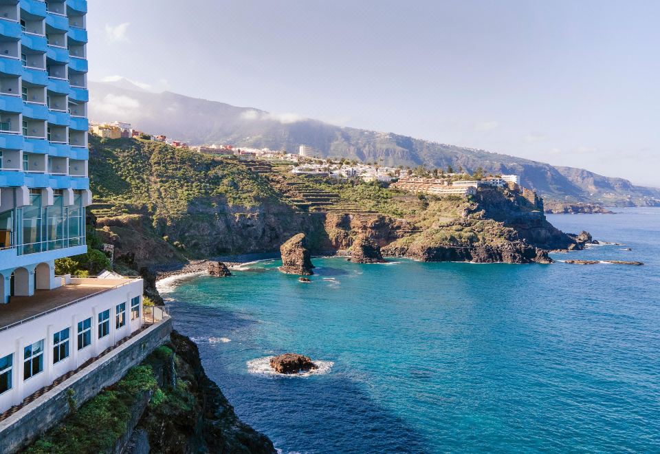 a beautiful coastal view with clear blue water , mountains in the background , and buildings perched on the cliffs at Precise Resort Tenerife