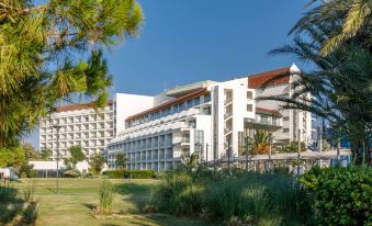a large white building surrounded by green grass and trees , located in a sunny location at Grand Hotel Ontur Cesme