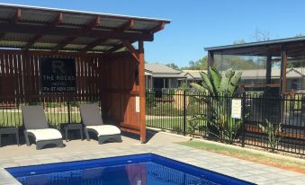 a swimming pool surrounded by a wooden deck , with lounge chairs and umbrellas placed around the pool area at The Rocks Motel