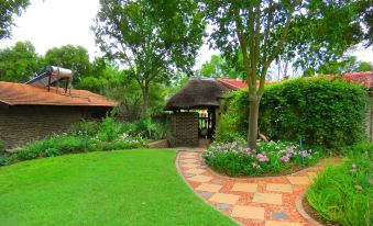 a well - maintained garden with lush greenery , a path , and a gazebo surrounded by flowers and trees at Pine Valley Lodge