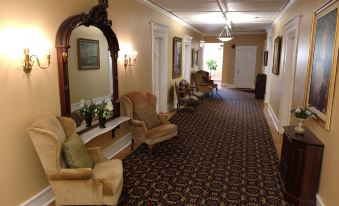 a long , carpeted hallway with white walls and wooden trim , featuring two large mirrors and two plush chairs at Thayers Inn