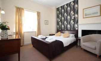 a large bed with a brown headboard is in a room with a window and a desk at Blue Bell Hotel