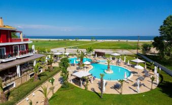 a large resort with multiple swimming pools , sun loungers , and umbrellas surrounded by green grass and trees near the ocean at Mediterranean Village Hotel & Spa