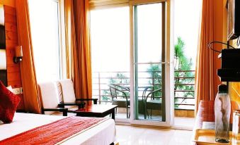 a well - lit hotel room with a large bed , a tv , and a balcony overlooking the city at Wood Stock Kasauli - Rooms & Cottages - Panoramic View & Balcony Rooms