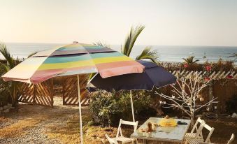 a colorful striped umbrella is set up over a dining table and chairs in a garden area near the ocean at Casa del Mar