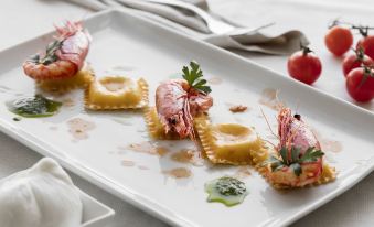 a white plate with a variety of seafood , including shrimp , pasta , and tomatoes , placed on a dining table at Hotel Belvedere