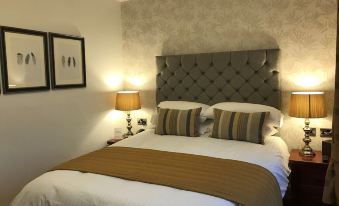 a neatly made bed with a tufted headboard and two lamps on either side of the bed at Loftsome Bridge Hotel