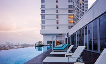 a large pool is surrounded by lounge chairs and a tall building in the background at DoubleTree by Hilton Melaka