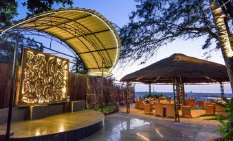 a tropical outdoor area with a large yellow structure , umbrellas , and tables under the evening sky at Beleza by the Beach
