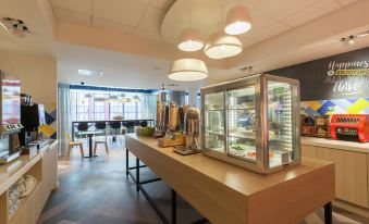 a modern cafe with a counter , glass display case , and multiple hanging lights , creating an inviting atmosphere at Hampton by Hilton Antwerp Central Station