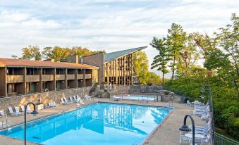 a large outdoor swimming pool surrounded by a hotel building , with several people enjoying their time in the pool at General Butler State Resort Park