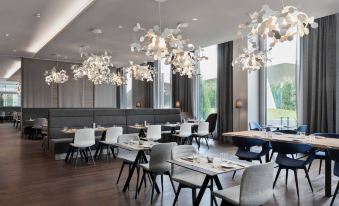 a modern restaurant with multiple dining tables and chairs , surrounded by large windows and chandeliers at Courtyard Munich Garching