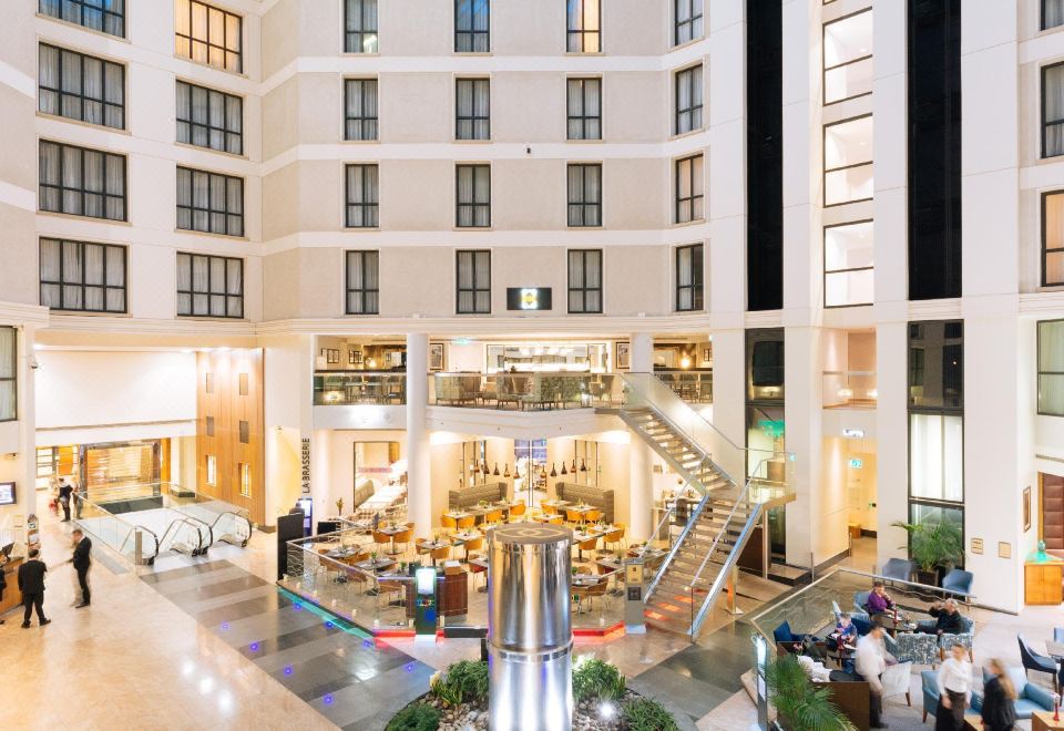a large hotel lobby with a spiral staircase leading to the second floor , where several people are gathered to enjoy a meal at Sofitel London Gatwick