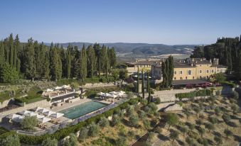 an aerial view of a resort with a large pool surrounded by trees , mountains in the background , and a mountain range in the distance at Rosewood Castiglion del Bosco