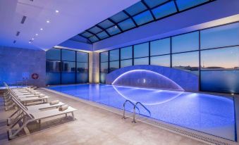an indoor swimming pool with a large window , surrounded by lounge chairs and a balcony at Doubletree by Hilton Istanbul Umraniye