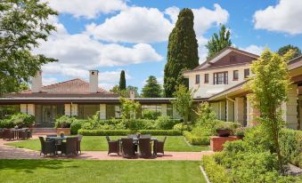 a lush green lawn surrounded by a brick patio , with several chairs and a dining table placed in the area at Hyatt Hotel Canberra - A Park Hyatt Hotel