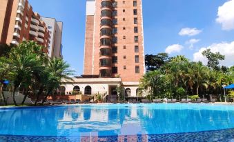 a tall building is reflected in a blue pool with palm trees in the background at Hotel Dann Carlton Medellín