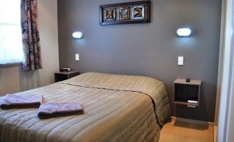 a bed with a beige blanket and two gray pillows is in a room with grey walls at Nambucca River Village by Lincoln Place