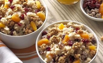 two bowls of oatmeal with granola , orange slices , and cranberries are placed on a wooden table at Home2 Suites by Hilton Marysville
