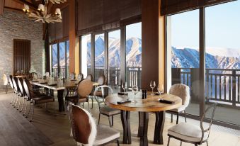 a dining room with wooden tables and chairs , along with a view of snow - covered mountains outside the window at Park Chalet, Shahdag, Autograph Collection
