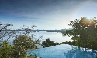 a large , blue swimming pool surrounded by trees and mountains , with the sun setting in the background at Heritance Kandalama