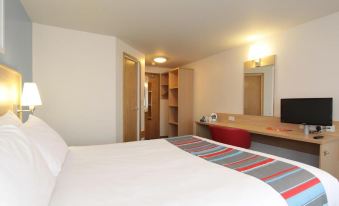 a large bed with white sheets is in a room with a desk and bookshelves at Travelodge Stafford M6