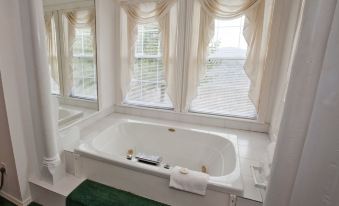 a white bathtub with a green rug and towel rack in front of large windows at The Bradford