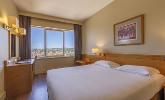 a large bed with white sheets is in a hotel room with a window overlooking a city at Hotel Fundador