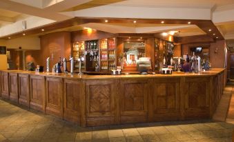 a bar with a wooden counter , several bottles of beer , and a few cups on the counter at Premier Inn Tamworth South