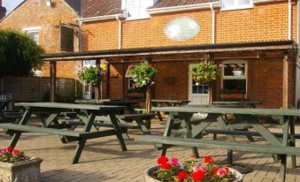 a brick building with a red tile roof , surrounded by wooden picnic tables and benches at The Foxham