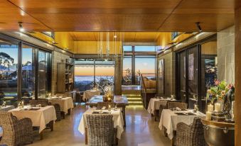 a restaurant with a large dining table and chairs , surrounded by windows offering a view of the ocean at Spicers Sangoma Retreat