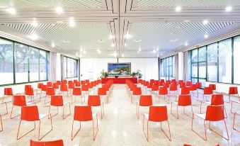 a large , empty conference room with rows of red chairs arranged in front of a stage at Arbatax Park Resort - Telis