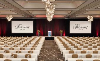 a large , empty conference room with rows of white chairs and a stage at the front at Fairmont Dallas