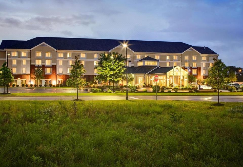 a large hotel surrounded by trees and grass , with the lights from nearby lights illuminating the building at Hilton Garden Inn Akron-Canton Airport