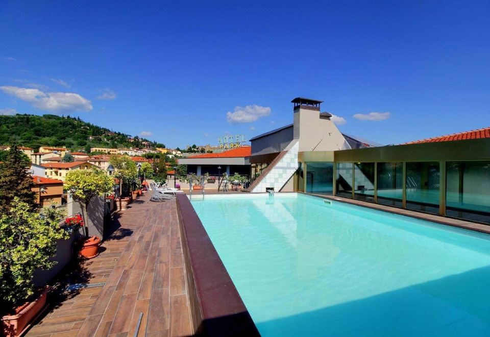 an outdoor swimming pool surrounded by a building , with people enjoying their time in the pool at Hotel Park