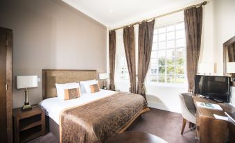 a large bed with a brown and white patterned comforter is situated in a room with two windows at Columba Hotel Inverness by Compass Hospitality